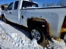 Rusty white pickup truck parked in snow with visible damage.