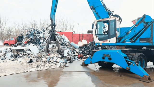 Blue crane lifting scrap metal at a recycling yard.
